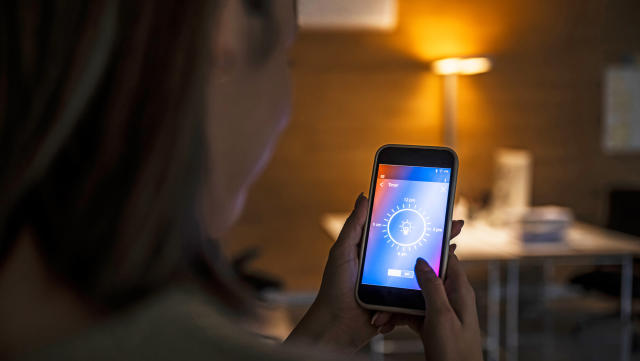 Woman using smart phone with light bulb icon screen at home.    