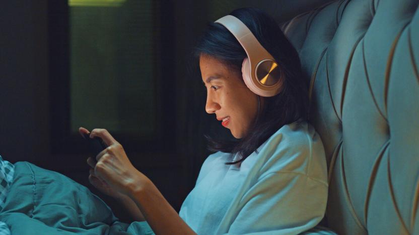 Young Asia girl media addiction on bed wear headphone laugh watch favorite movie in streaming online VOD, video on demand in home at night. Insomnia, Cybersickness, Nomophobia, sleep disorder concept.