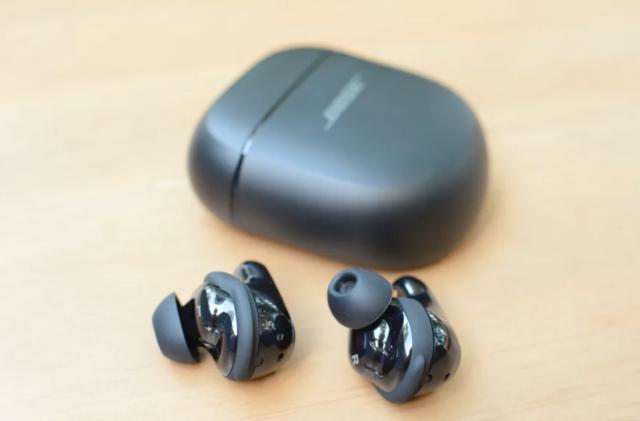 A pair of earbuds on a table next to a charging case. 