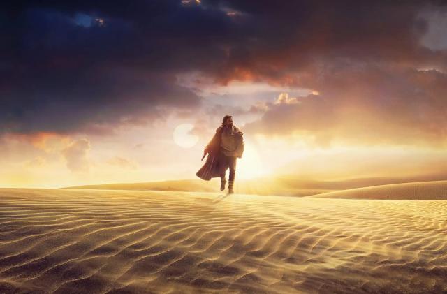 A still from the Disney+ show 'OBI-WAN KENOBI' showing Obi-Wan walking alone over sand dunes with dramatic dark clouds along with a bright late evening (or early morning) sun in the sky.