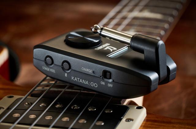 A headphone amp on top of a guitar.