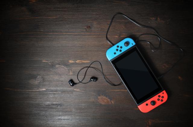 Minsk, Belarus - May 07, 2020: Nintendo Switch game console with black screen and bright joy-con controllers on wood table background. Copy space for text. Top view. Flat lay.