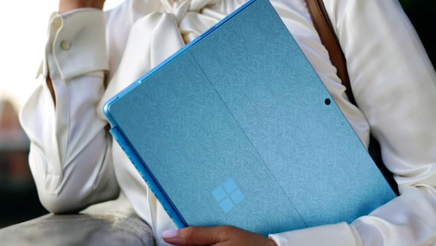 Lifestyle image of the Microsoft Surface Pro 9. A person holds a blue (patterned) version of the hybrid device (back-facing).