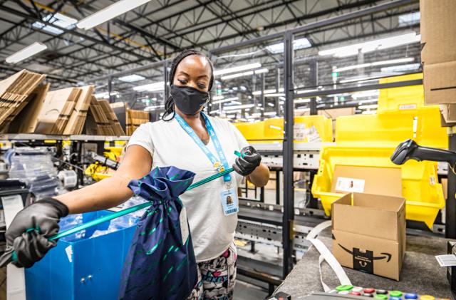 A woman packs an Amazon order. Amazon boxes with the company's arrow logo are scattered in the background.
