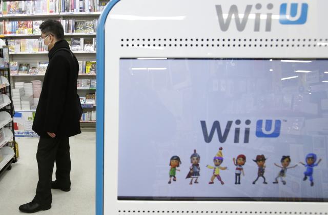 A shopper is seen behind a advertisement board of Nintendo Co Ltd's Wii U game console at an electronics retail store in Tokyo January 29, 2014. Nintendo Co Ltd, facing a third year of losses, is getting lots of unsolicited advice on how to squeeze more out of its Mario franchise and revive its fortunes after admitting that its Wii U game console has been a flop. REUTERS/Yuya Shino (JAPAN - Tags: BUSINESS SCIENCE TECHNOLOGY)