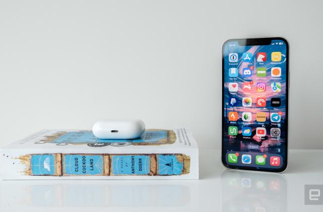 An iPhone 12 next a blue and white book and a pair of AirPods Pro. 