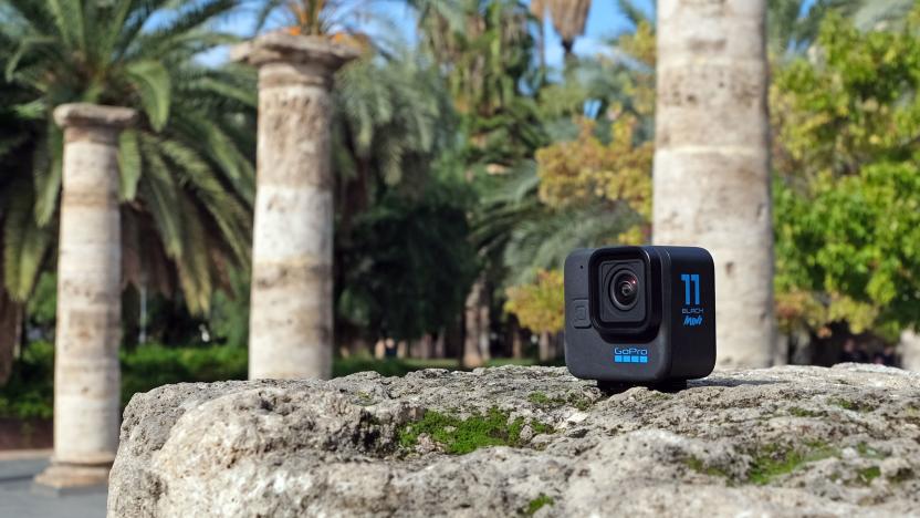 The GoPro Hero 11 Black Mini pictured on a rocky surface in a park with roman-style columns and palm trees in the background.