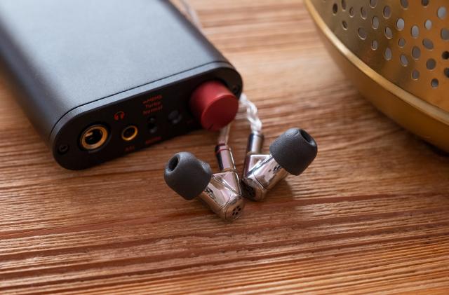 A pair of silver headphones are pictured infront of a hi-fi DAC on top of a coffee table.