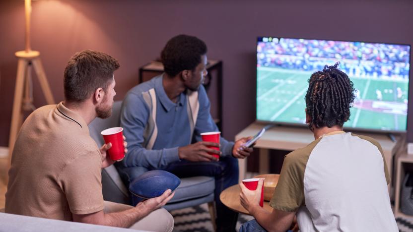 Back view at diverse group of friends watching American football match on TV at home