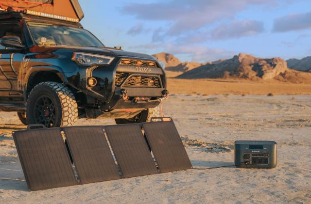An SUV parked in a remote desert-like area has the BioLite BaseCharge 1500 and SolarPanel rigged to collect a charge from the sun.