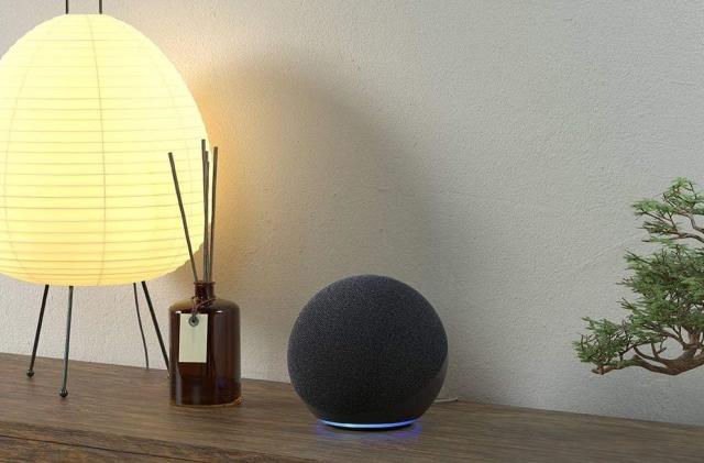 An Echo Show sits on a wooden table beside a diffuser and lamp.
